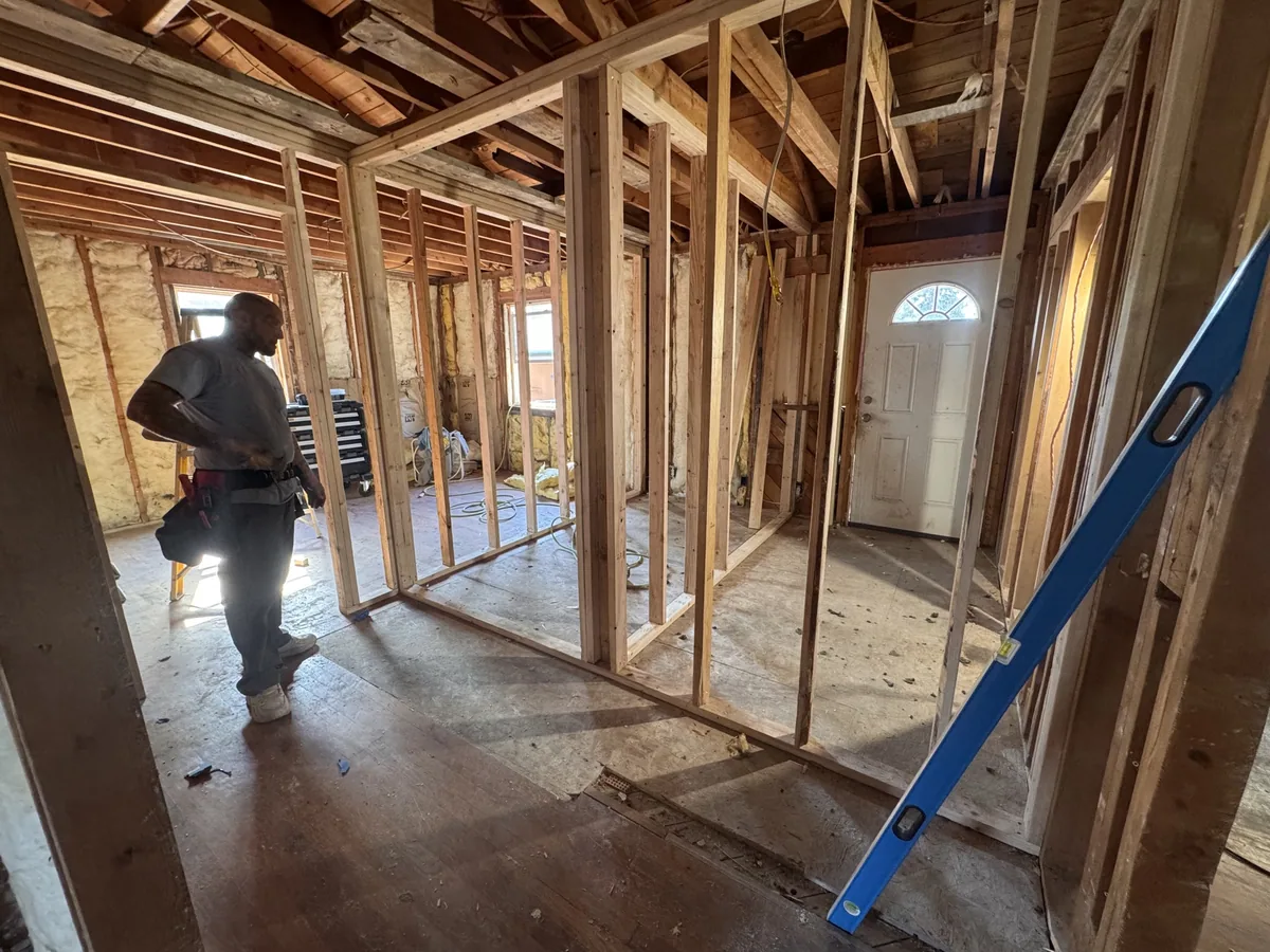 New interior stud walls being framed in a gut remodel, carpenter working with a level standing by
