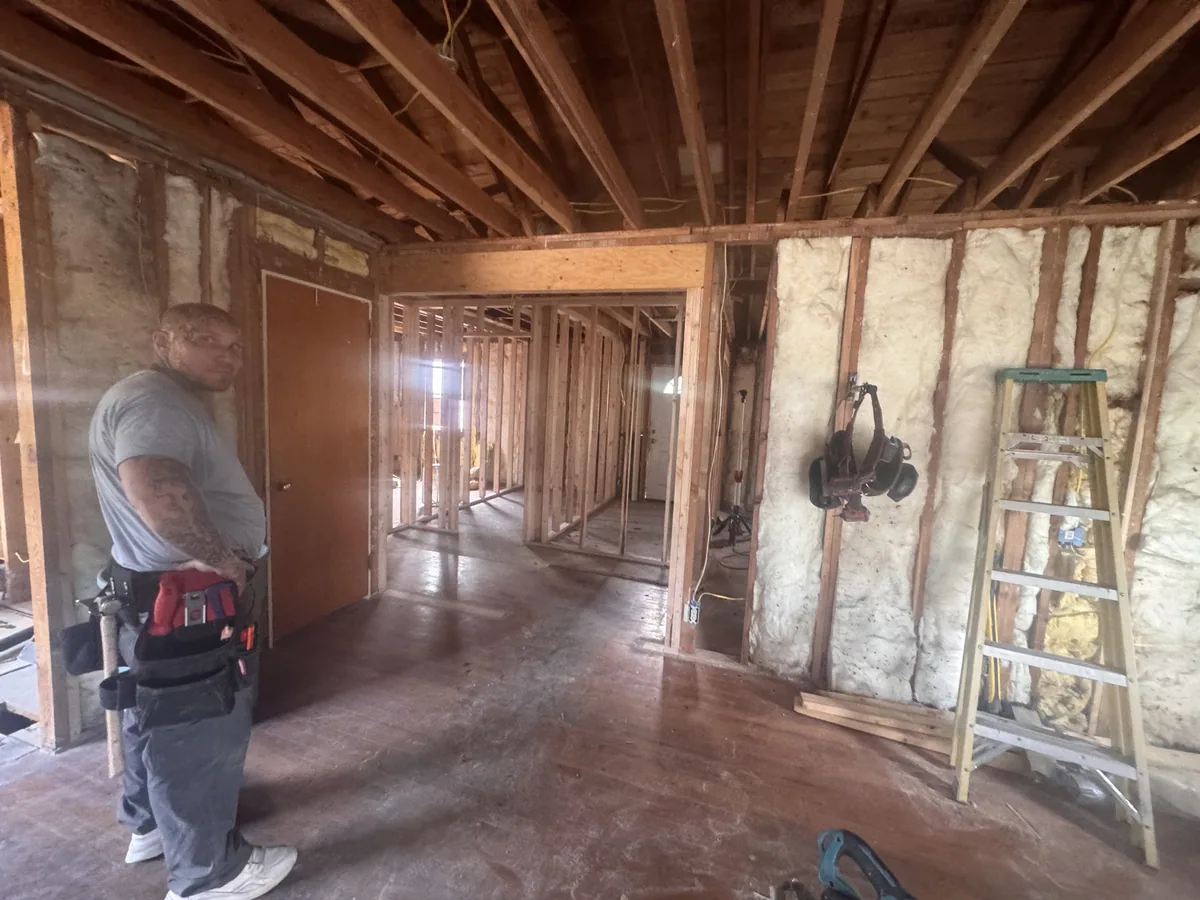 Interior framing in progress with stud walls, insulation and a ladder in a stripped house