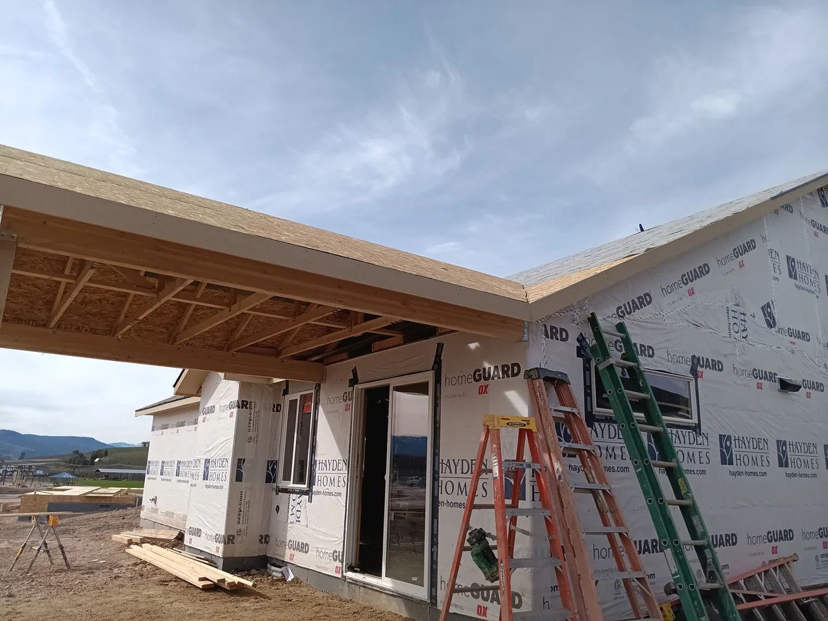 Covered patio framing on a new home, ridge beam and rafters cut and set, house wrapped behind