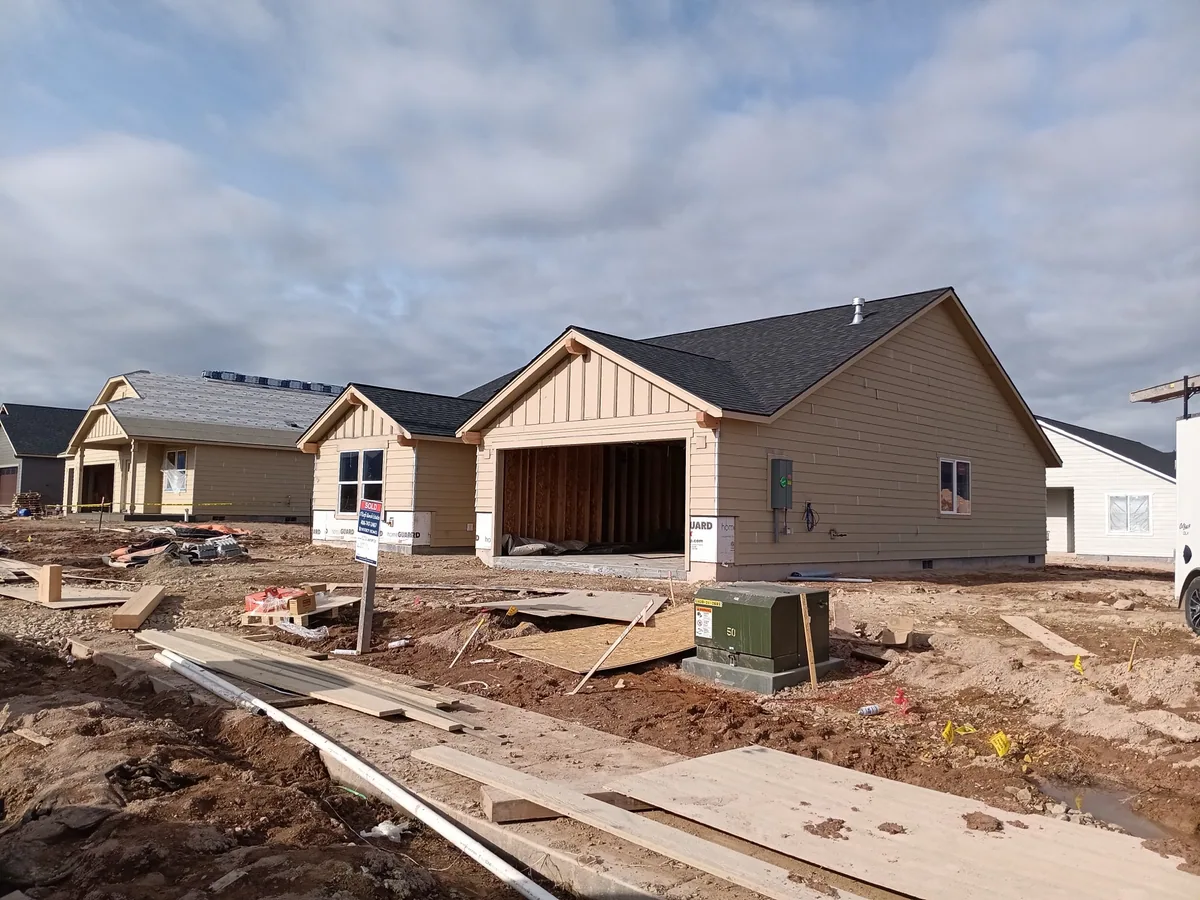 Two nearly finished new homes side by side in a subdivision with dirt yards