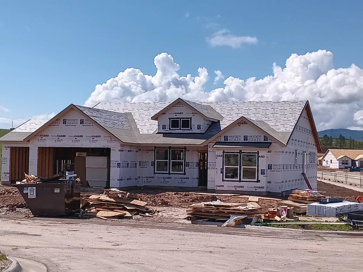 A new home framed, sheathed and shingled, wrapped and ready for siding under a big Montana sky