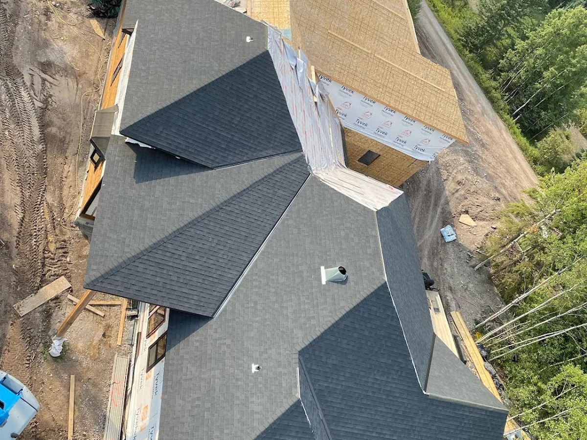 Overhead view of a finished shingled roof with multiple hips and dormers on a house still under construction