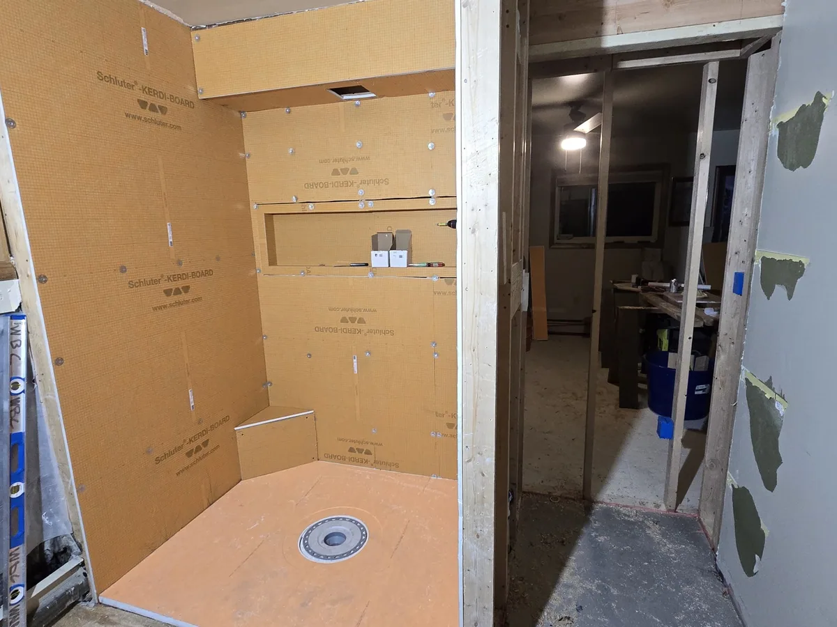 A shower alcove framed and waterproofed with a sloped pan, bonded drain and a built-in recessed niche